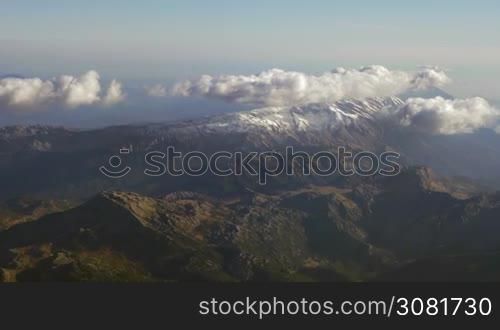 Looking at landscape from flying airplane. Aerial panorama of vast mountain range with clouds over the tops