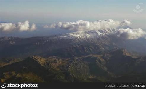 Looking at landscape from flying airplane. Aerial panorama of vast mountain range with clouds over the tops