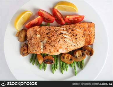 looking down on a plate of pan-fried salmon fillet served on a bed of asparagus with tomatoes and mushrooms