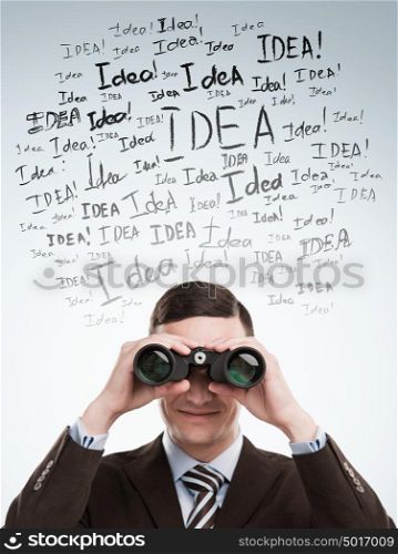 Looking for Ideas concept. Young business man standing on gray background with with binoculars idea signs in front