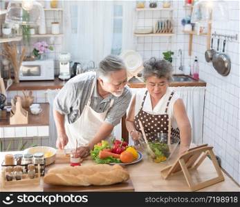 Looking for new recipes. Asian senior elderly couple using digital tablet at kitchen, enjoying cooking together at home in leisure time.