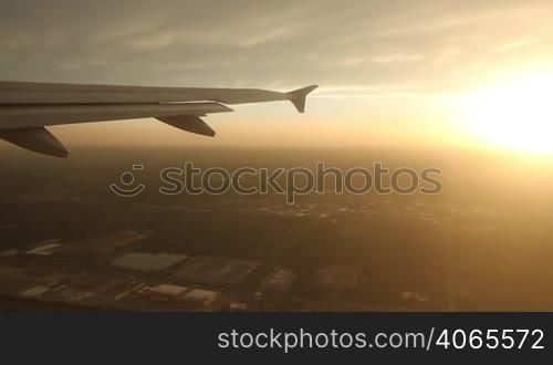 Looking out the window at the wing of an airborne jet, with a brilliant sunset in the distance