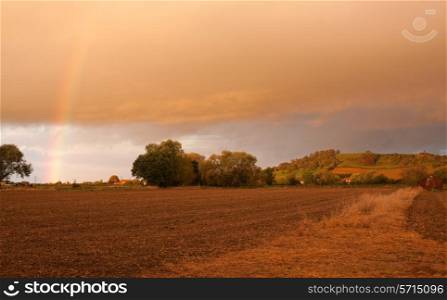 Looking towards Meon Hill over farmland with a dramatic sunset and rainbow, Gloucestershire, England.