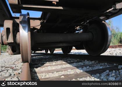 looking up at a rusty freight train car with wheels polished to a shiny finish by the railroad tracks underneath