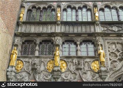 Looking up at medieval guilded statues and windows of the Basilica of the Holy Blood. Burg Square, Bruges, West Flanders, Belgium, Europe