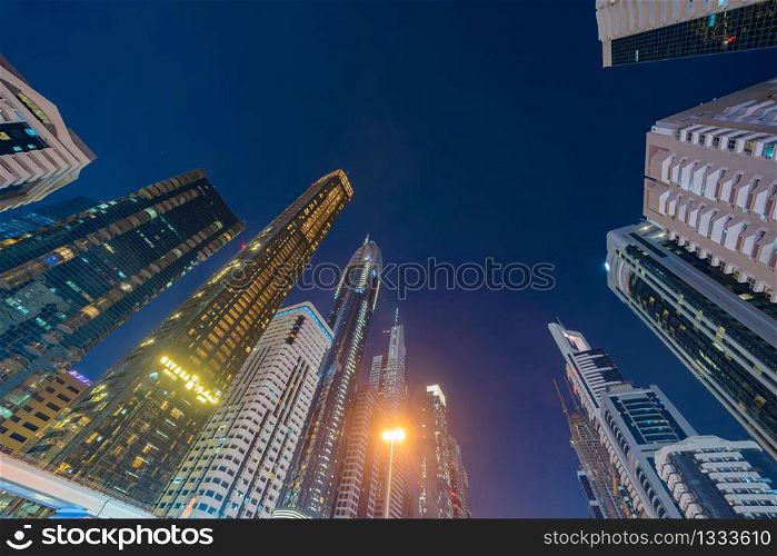 Looking up to high-rise office buildings, skyscrapers, architectures in financial district. Smart urban city for business and technology concept background in Downtown Dubai, UAE at night.
