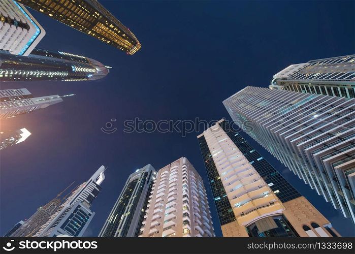 Looking up to high-rise office buildings, skyscrapers, architectures in financial district. Smart urban city for business and technology concept background in Downtown Dubai, UAE at night.