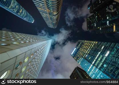Looking up to high-rise office buildings, skyscrapers, architectures in financial district. Smart urban city for business and technology concept background in Downtown Hong Kong at night.