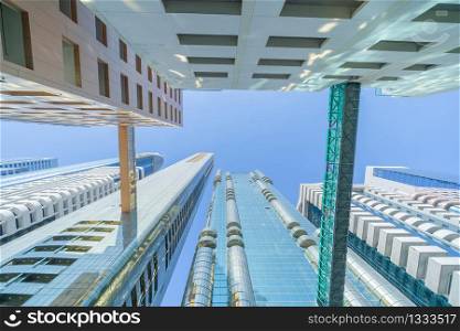 Looking up to high-rise office buildings, skyscrapers, architectures in financial district with blue sky. Smart urban city for business and technology concept background in Downtown Dubai, UAE.