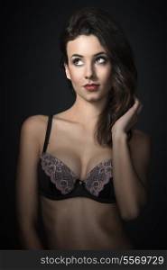 looking up young beautiful sexy girl wearing a fashion bra , and posing on dark background. she has hairstyle
