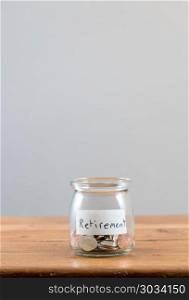 Loose change inside glass jar to represent retirement savings . Loose change and coins inside a glass jar against a grey background to represent lack of retirement savings. Loose change inside glass jar to represent retirement savings