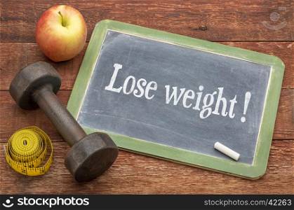 Lose weight concept - slate blackboard sign against weathered red painted barn wood with a dumbbell, apple and tape measure