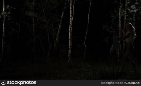 Lost beautiful young woman in shorts is attacked by sexual maniac in dark forest at night. Innocent victim fighting with the attacker in dark birch grove in night time. Sexual violence. Slow motion.