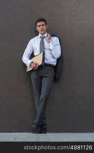 Lost in business thoughts. Thoughtful businessman in formalwear holding documents and looking away while standing against grey wall background