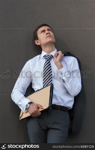 Lost in business thoughts. Thoughtful businessman in formalwear holding documents and looking away while standing against grey wall background