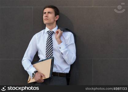 Lost in business thoughts. Thoughtful businessman in formalwear holding documents and looking away while standing against grey wall background
