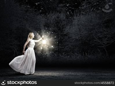 Lost in darkness. Young woman with lantern walking in dark forest