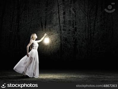 Lost in darkness. Young woman with lantern walking in dark forest