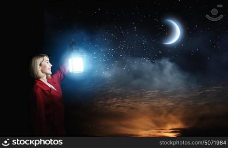 Lost in night. Young blond woman in red cloak with lantern