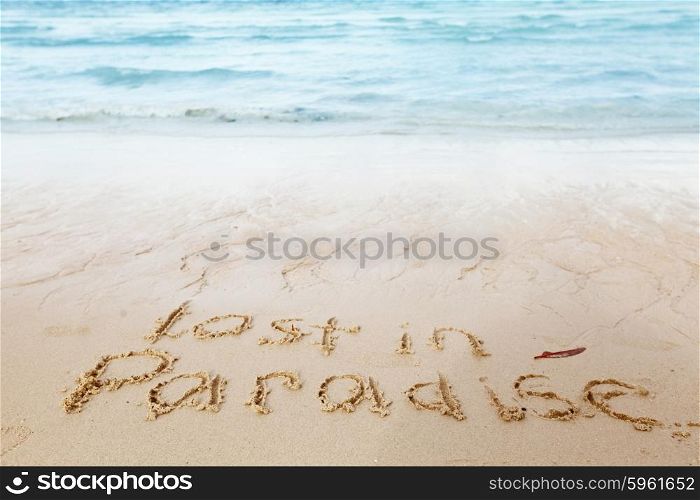 Lost in paradise concept. Lost in paradise concept - inscription on a beach sand with coming wave