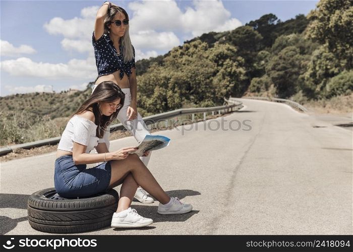 lost woman sitting tire with her friend looking map