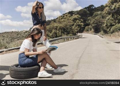 lost woman sitting tire with her friend looking map