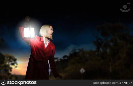 Lost woman. Young blonde in red cloak with lantern in darkness