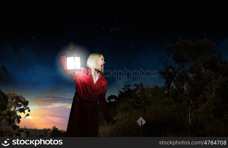 Lost woman. Young blonde in red cloak with lantern in darkness