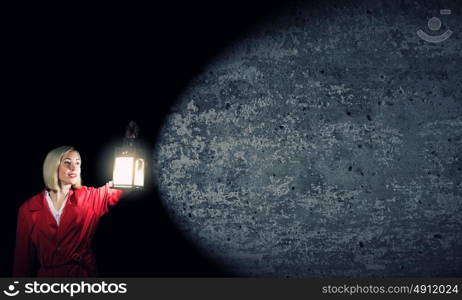 Lost woman. Young blonde in red cloak with lantern in darkness