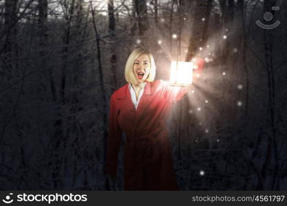 Lost woman. Young blonde in red cloak with lantern in night forest