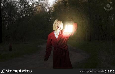Lost woman. Young blonde in red cloak with lantern in night forest