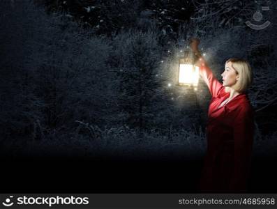 Lost woman. Young blonde in red cloak with lantern in night forest