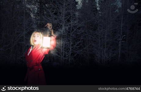 Lost woman. Young blonde in red cloak with lantern in night forest