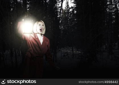 Lost woman. Young blonde in red cloak with lantern in night forest