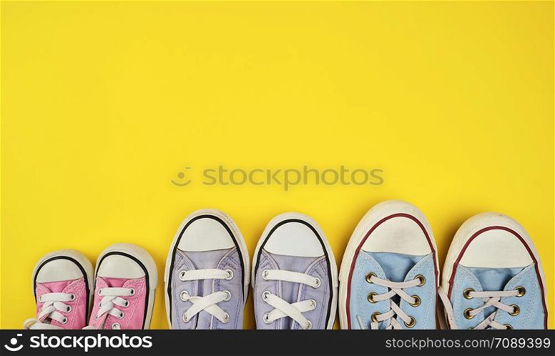 lot of textile worn sneakers of different sizes on a yellow background, empty space , family concept