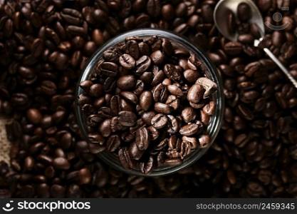 Lots of roasted coffee beans scattered on the table and in a glass jar. Focus on freshly roasted coffee beans in a jar, top view