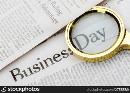 Loupe lies on the newspaper with title Business day. A photo close up. Selective focus