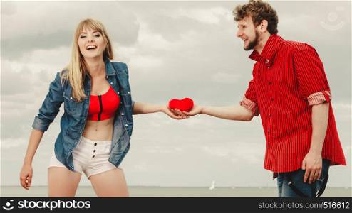 Love and happiness concept. Woman and man young hipster couple in love playing sharing free time having fun holding red heart, outdoor against sky