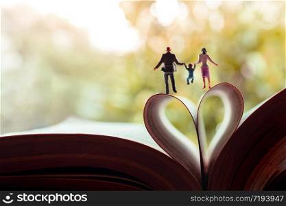 Love and Happy Family. Work Life Balance Concept. Miniature of Father, Mother and Son holding Hands and Walking toward the Book over a Page Roll like Heart Shape