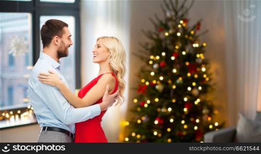 love and holidays concept - happy couple hugging over home room with christmas tree background. happy couple hugging at home on christmas