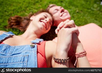 love and people concept - close up of happy teenage couple lying on grass and holding hands with wristbands at summer. happy teenage couple lying on grass at summer