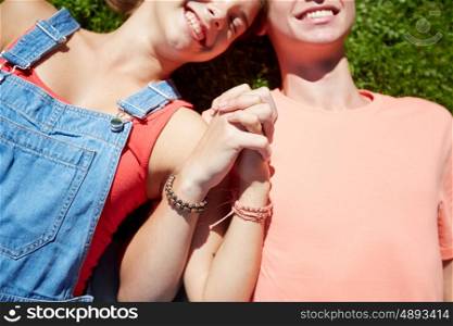 love and people concept - close up of happy teenage couple lying on grass and holding hands with wristbands at summer. happy teenage couple lying on grass at summer