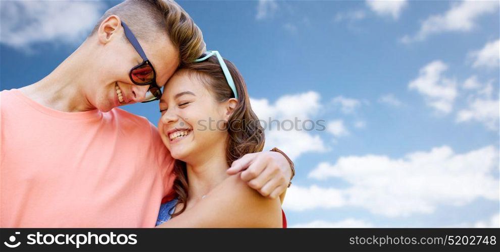 love and people concept - happy smiling teenage couple hugging at summer over blue sky and clouds background. happy teenage couple hugging over blue sky