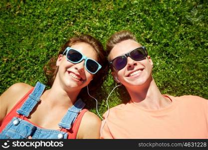 love and people concept - happy teenage couple in sunglasses lying on grass with earphones and listening to music at summer. happy teenage couple with earphones lying on grass