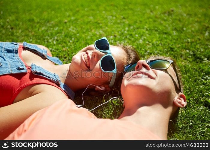 love and people concept - happy teenage couple in sunglasses lying on grass with earphones and listening to music at summer. happy teenage couple with earphones lying on grass