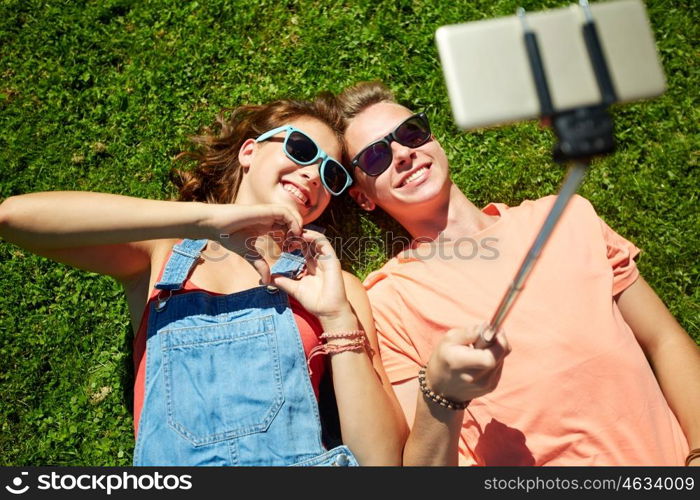 love and people concept - happy teenage couple in sunglasses lying on grass and taking selfie on smartphone at summer. happy couple taking selfie on smartphone at summer