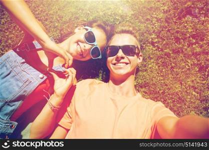 love and people concept - happy teenage couple in sunglasses lying on grass and taking selfie at summer. happy teenage couple taking selfie on summer grass