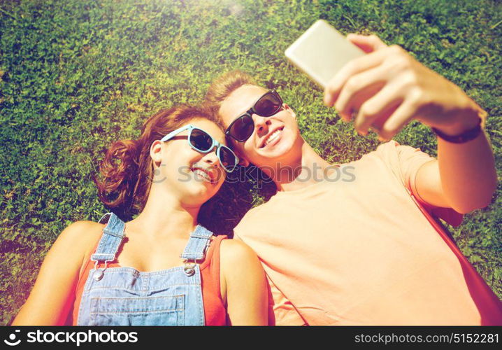 love and people concept - happy teenage couple in sunglasses lying on grass and taking selfie on smartphone at summer. happy couple taking selfie on smartphone at summer