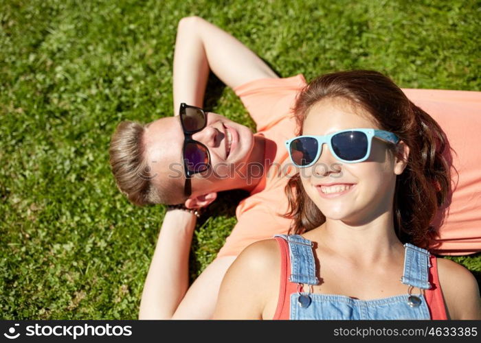 love and people concept - happy teenage couple in sunglasses lying on grass at summer. happy teenage couple lying on grass at summer