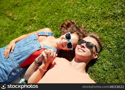 love and people concept - happy teenage couple in sunglasses lying on grass at summer. happy teenage couple lying on grass at summer